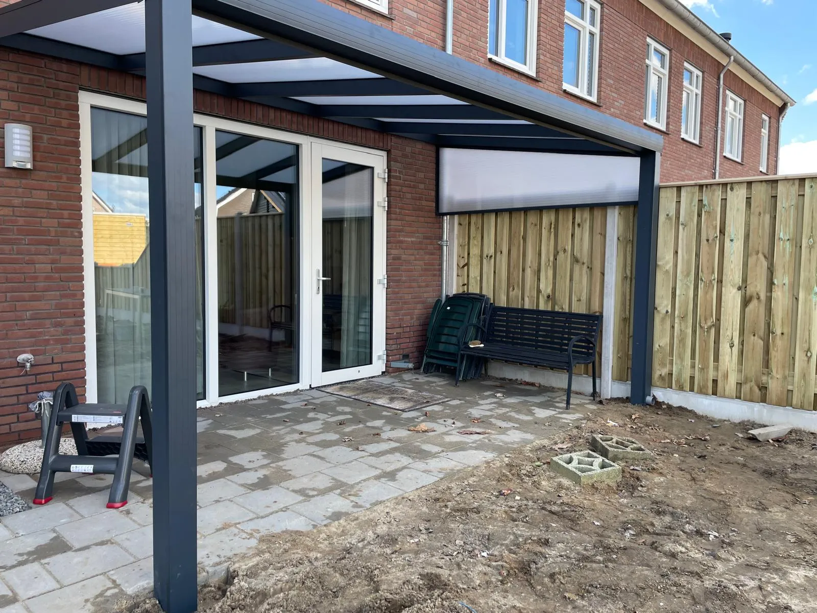 Antraciet veranda tegen een bakstenen rijwoning, net na de montage